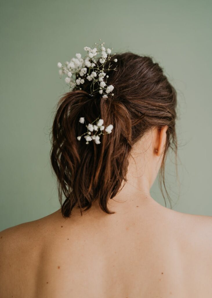 Woman's back view highlighting her hairstyle with delicate white flowers on a green background.