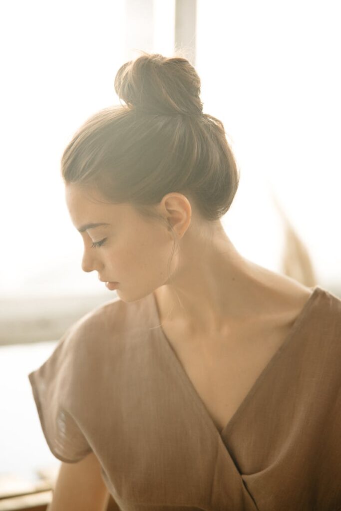 A serene portrait of a woman with a hair bun, captured in soft natural light indoors.