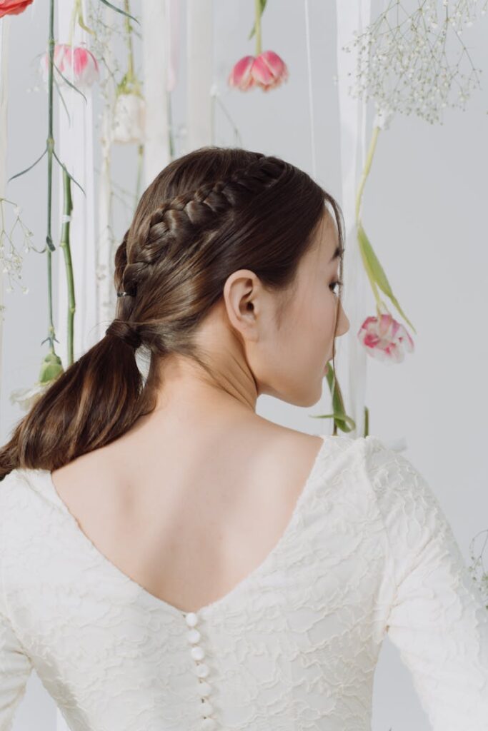 Back view of a bride with braided hair and floral backdrop, wearing an intricate wedding dress.